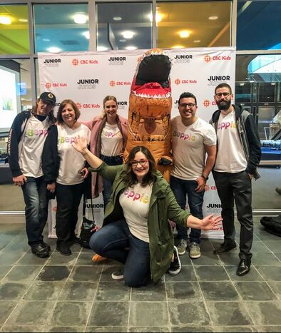 Beppie posing in front of an inflatable dinosaur after performing at the JUNIOR Junos in London, Ontario. She is surrounded by her mom and dad, and three of her co-workers.